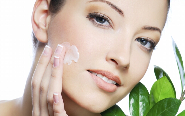 Woman applying moisturizer cream on face. Close-up fresh woman face.