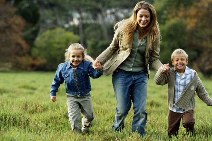 Mother walking with son and daughter (children 4-6) in field, smiling