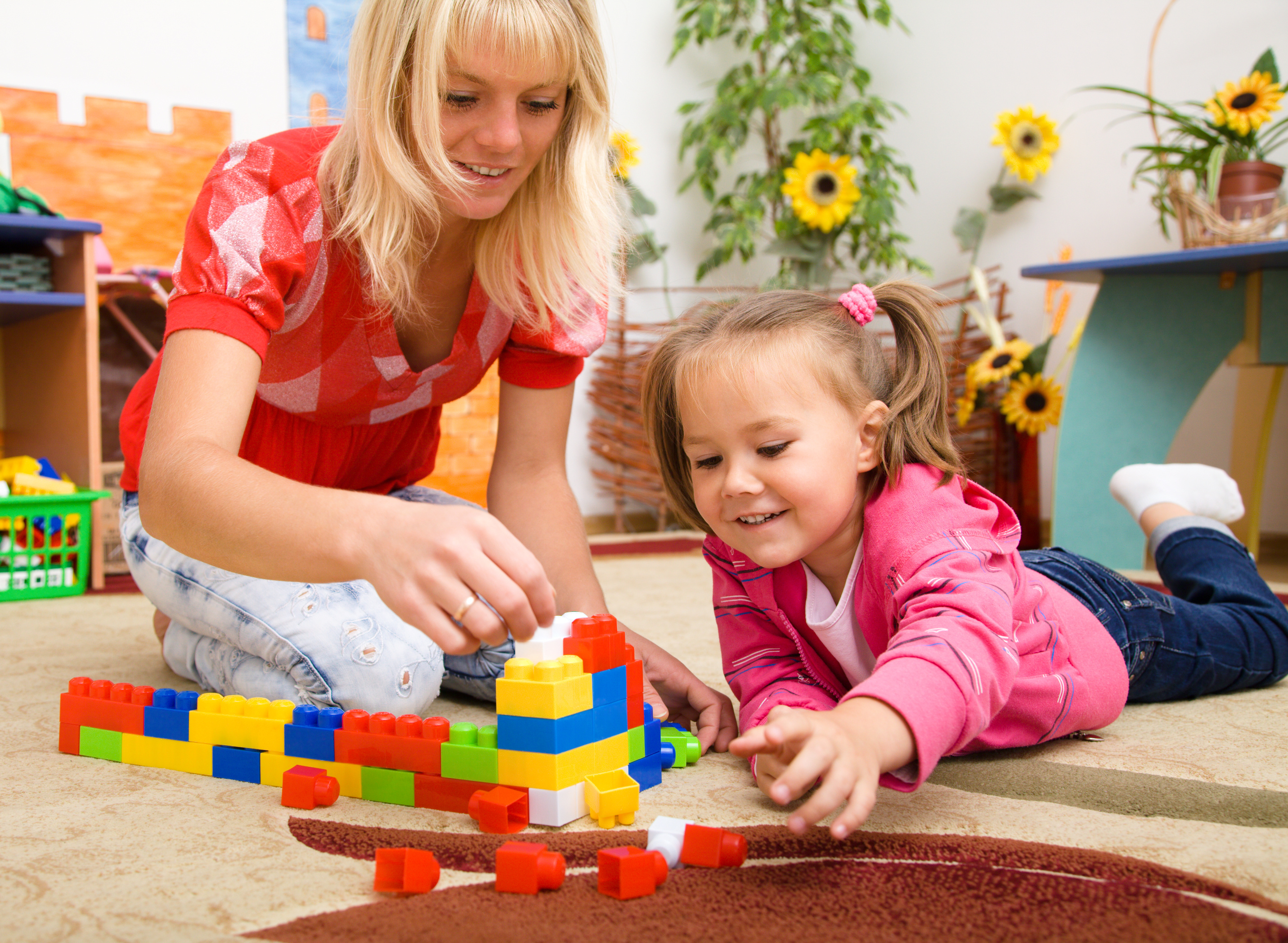 Teacher and child are playing with building bricks in preschool